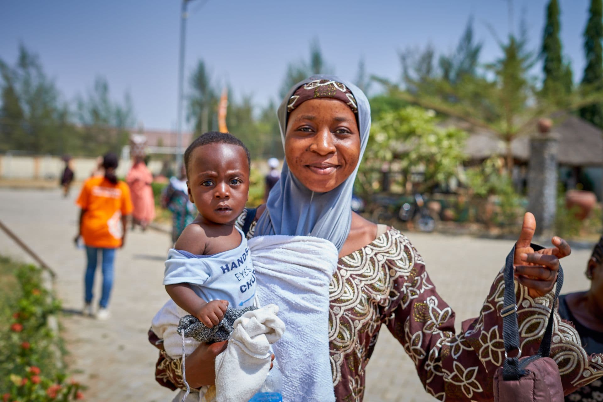 A smiling mother holds her baby outdoors in Keffi, Nigeria.